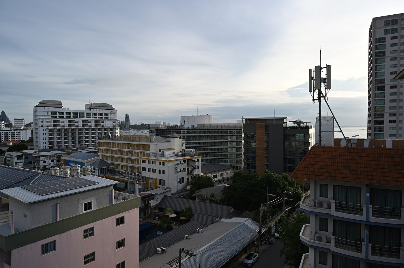 Low-rise hotels and apartment buildings along a Na Kluea street in Pattaya with the Gulf of Thailand behind, typical short-stay rental housing for expats renting in Thailand.