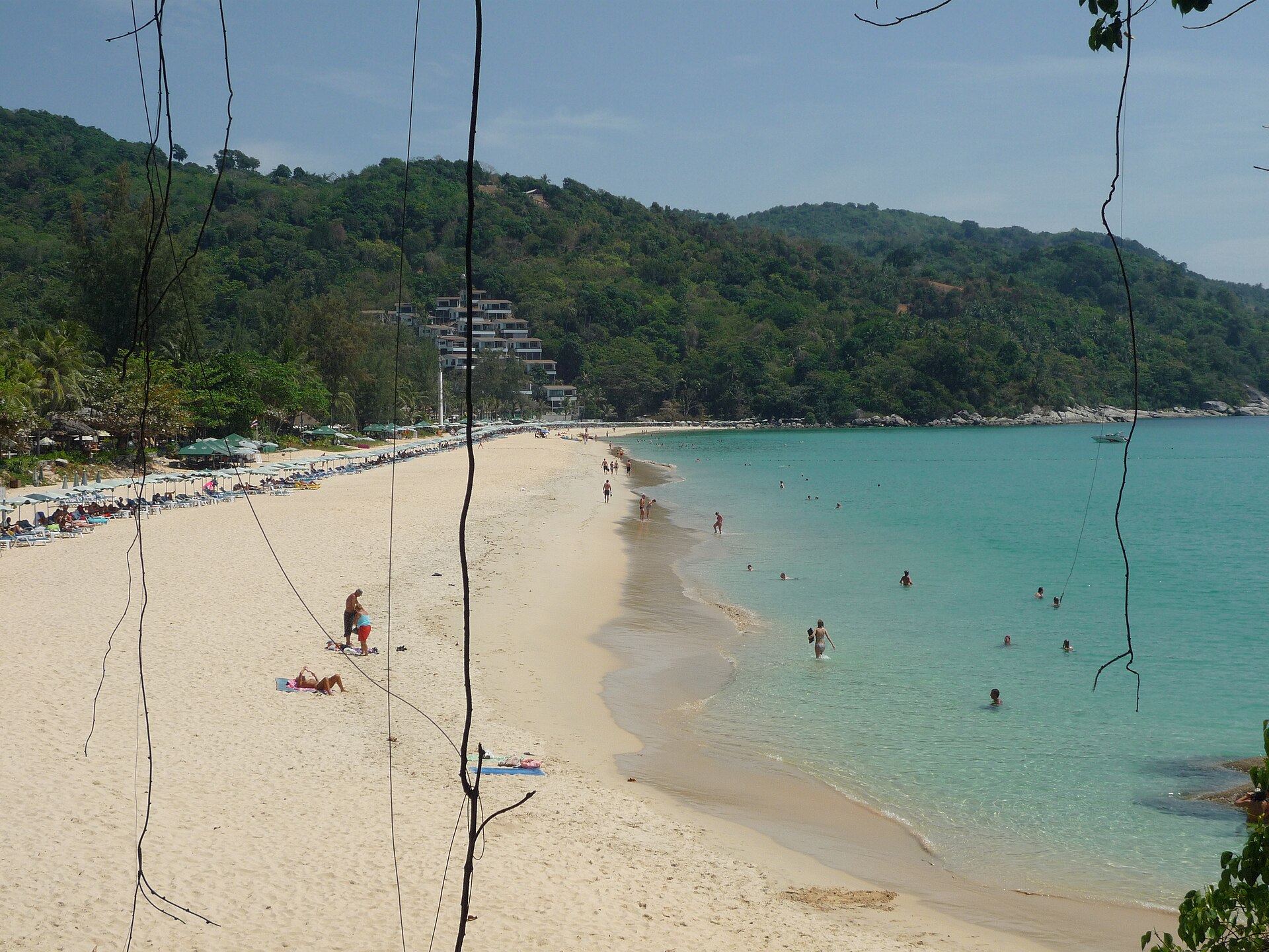 Kata Beach in Phuket seen from a headland, with white sand, turquoise water and a terraced hillside condo development among the trees, typical of the property foreigners weigh when planning a Thailand long stay.