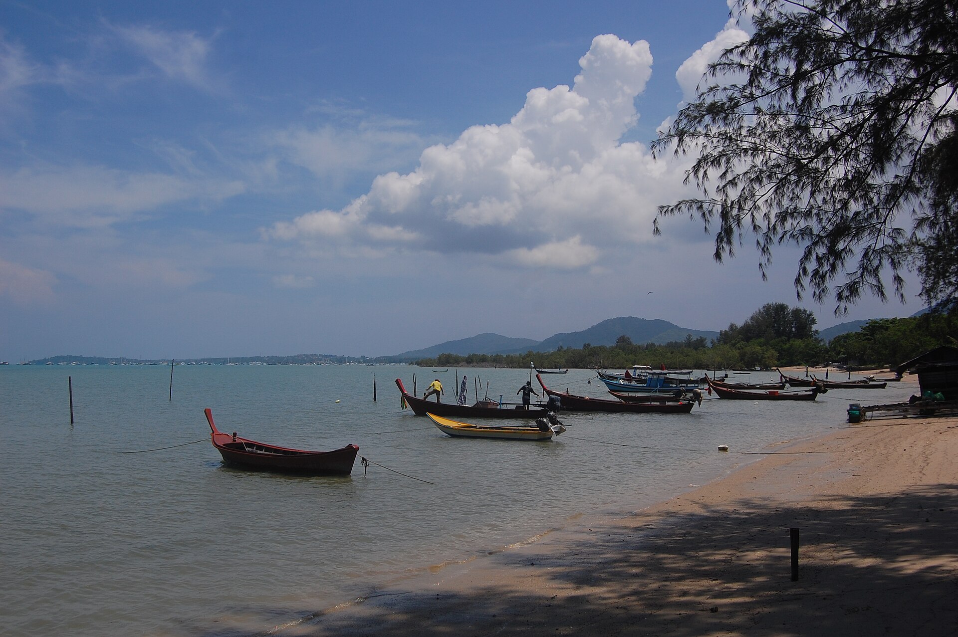 Traditional wooden longtail boats moored in shallow water at Palai Bay, Phuket, with hills and the yacht-filled Chalong Bay on the horizon, a quieter side of Phuket for expats on a Thailand long stay.