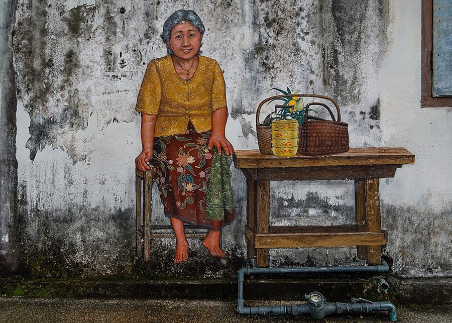 Hand-painted street mural of an elderly woman beside a table in Phuket Town, an everyday scene of living in Thailand where an overstaying Thai visa holder went unnoticed for years.