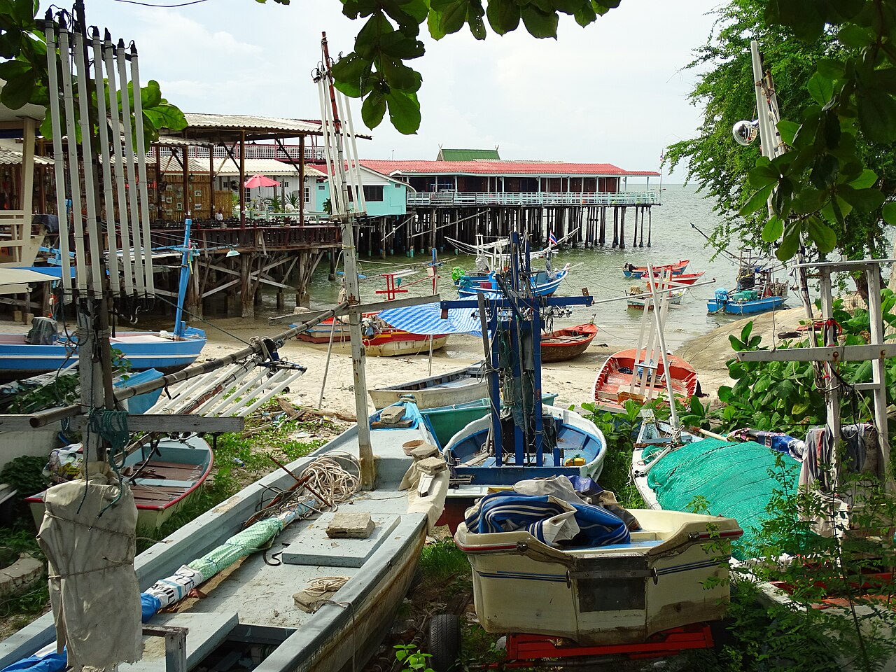 Fishing boats on the sand below stilted seafront restaurants in Hua Hin, Thailand, the kind of waterfront buildings at risk as living in Thailand beachfront rules tighten